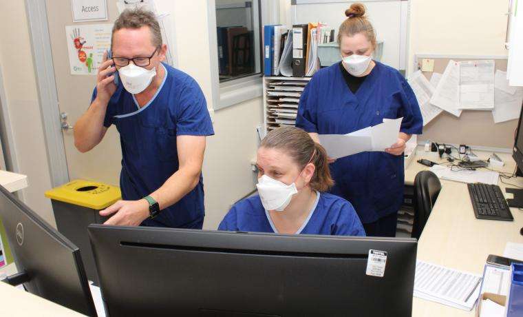 Hospital In The Home – COVID Home Monitoring Program Nurse Unit Manager Liam Nancarrow discusses a case with Ward Clerk Jess O’Mahony, as Registered Nurse Laura Marshall consults patient notes.