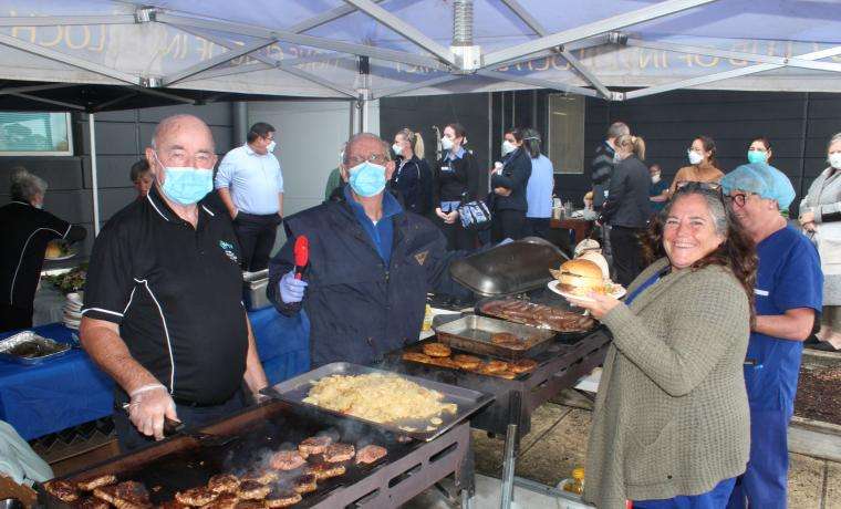 BCH Inverloch Fundraising Auxiliary members Klaus Edel (left) and Terry Hall serve Bass Coast Health Nurse Jane Ori at the staff barbecue at Wonthaggi Hospital.