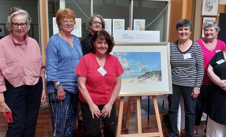 Inverloch Art Auxiliary Committee members including, from left, Lyne Hodges, curator Susan Hall, curator Ursula Theinert, Jane Hudson, Lynne Jansen, Maria McDonald and President Deb Watson with the major art raffle prize, Clouds over Bass Coast, by Adrian Johnson. Absent: curator Karen Ellis, and committee members Sarah Spencer-Smith, Amanda Watts and Tessa Hubble.