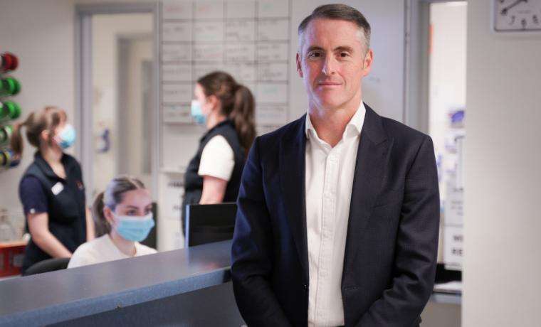 Adam Horsburgh in the foreground, with three Alfred Health staff slightly blurred in the background.