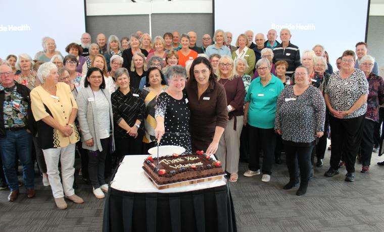 Paula Rogers, who has volunteered at the San Remo Op Shop for 20 years, joins Volunteer and Fundraising Manager Kerry Redmond and volunteers and staff in cutting a cake to celebrate National Volunteer Week.