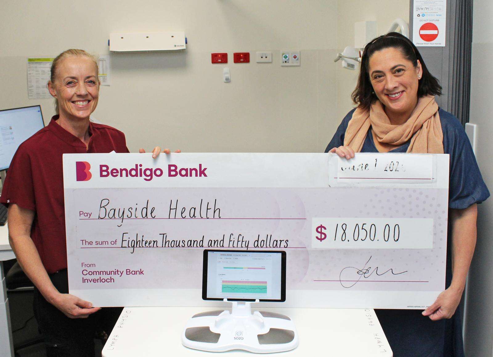 Bayside Health Regional Lymphoedema Practitioner Michelle McMahon and Fundraising and Volunteer Manager Kerry Redmond hold the cheque in front of the Sozo Machine.