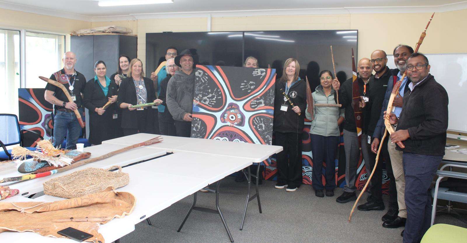 Staff at Kooweerup Hospital with the artwork they created with First Nations artist Steve Parker, left of painting.