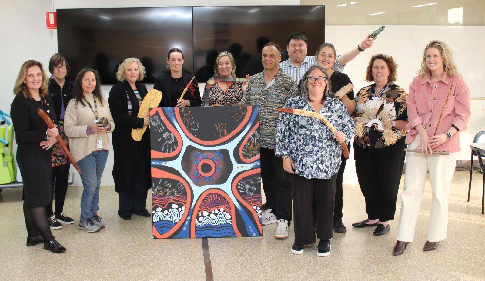 Wonthaggi Hospital staff display the artwork they made with First Nations artist Steve Parker, right of painting.